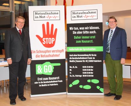 „Notaufnahme in Not“ –  Dr. Ulli Polenz (links im Bild) von der Kassenärztlichen Vereinigung informierte in der jüngsten Sitzung der Kommunalen Gesundheitskonferenz über die Kampagne, rechts im Bild Michael Beninde, stellvertretender Leiter der KGK, Gesundheits- und Ordnungsdezernent der Paderborner Kreisverwaltung Bildnachweis: Amt für Presse- und Öffentlichkeitsarbeit, Kreis Paderborn, Ulrike Sander 2 Männer vor Rollup